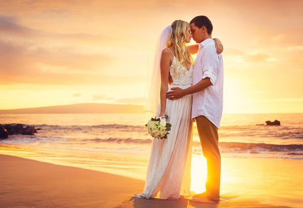 Wedding couple standing on beach with sun set in background