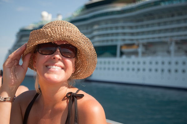 Picture of woman with sunglasses and hat on, with cruise ship behind her