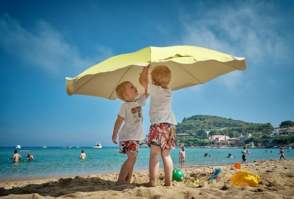 two boys putting up a small yellow umbrella on a sandy beach